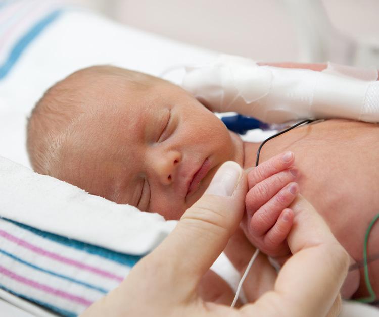 Mom holding the hand of her sleeping preemie