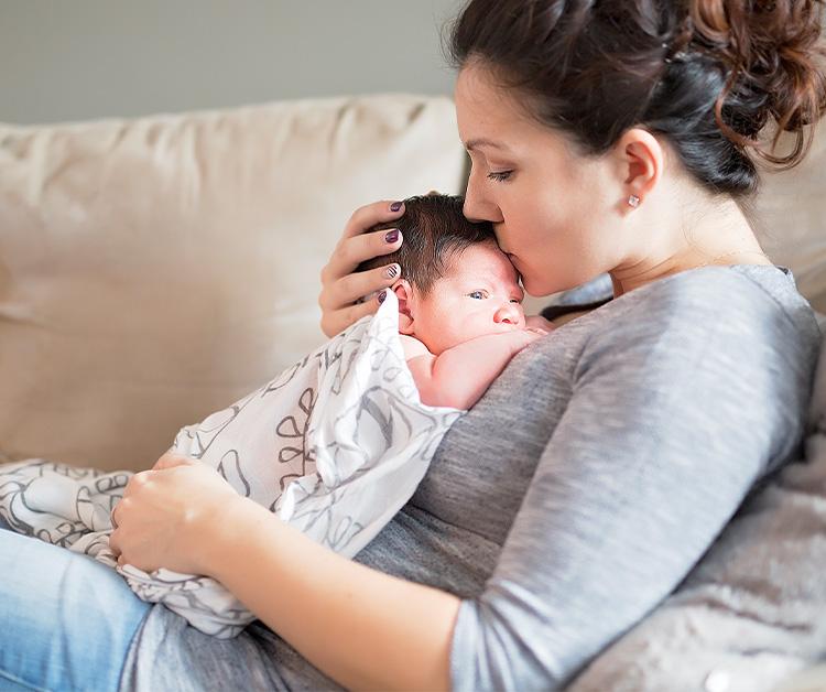 Mom snuggling her newborn baby while sitting on the couch