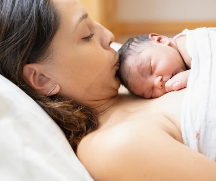 Una madre primeriza besando la cabeza de su bebé.