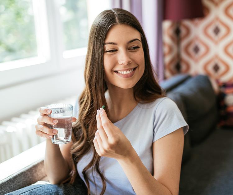 Smiling woman holding a glass of water and a vitamin