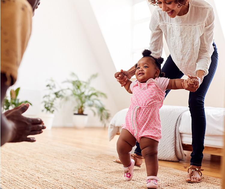 Parent helping toddler walk in the living room