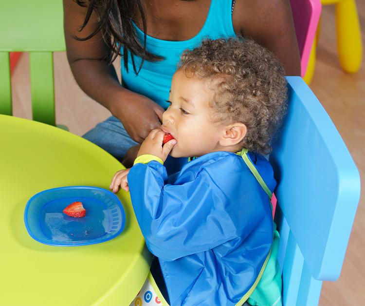 Toddler boy eating strawberries with his mom sitting by him