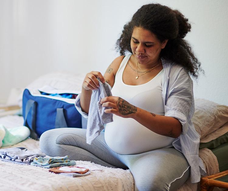 Pregnant woman packing baby clothes on bed