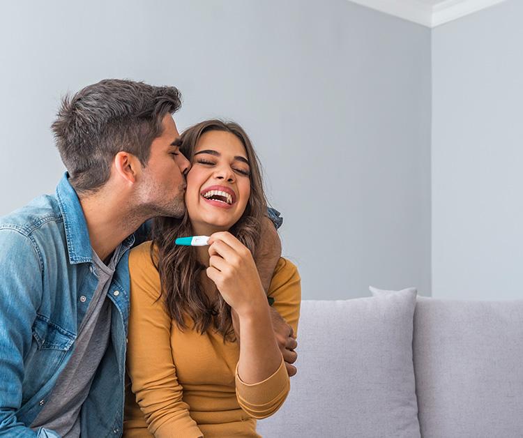 Husband kissing wife who's holding up a pregnancy test