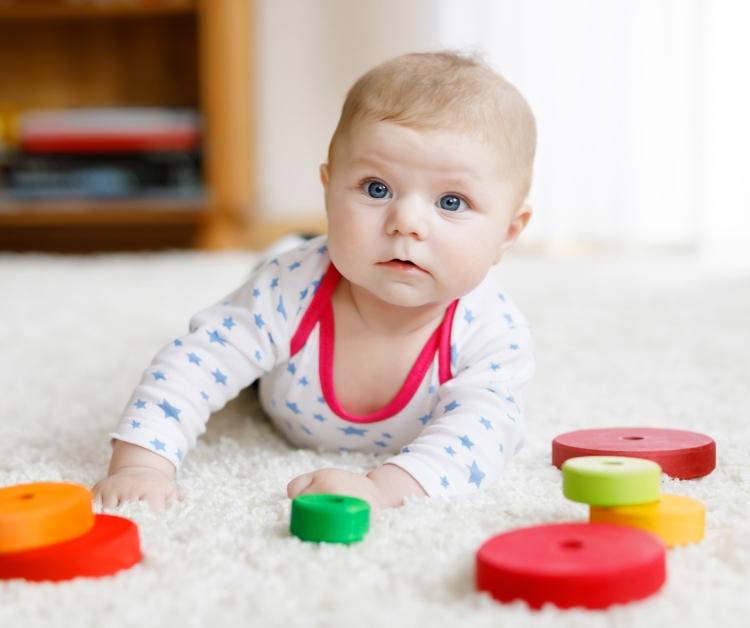 Baby laying on rug with toys
