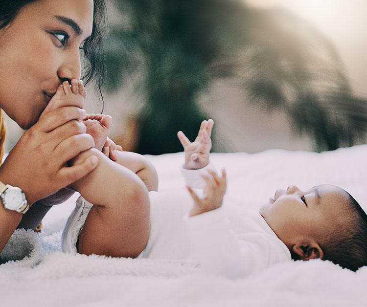 Mom with baby laying down and kissing baby's feet