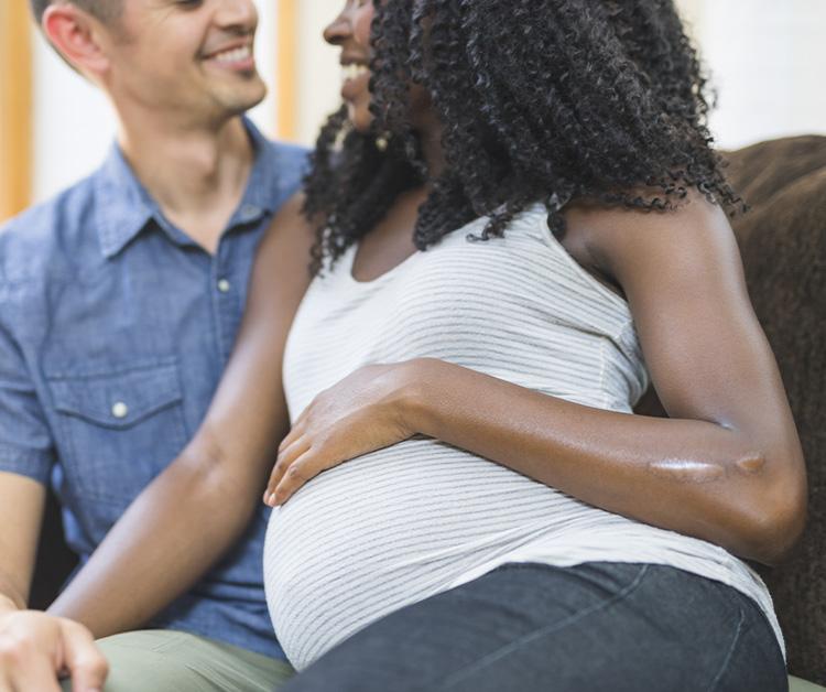 Mamá y papá sentados en un sofá con su hijo. El hijo besa el vientre embarazado de la mamá