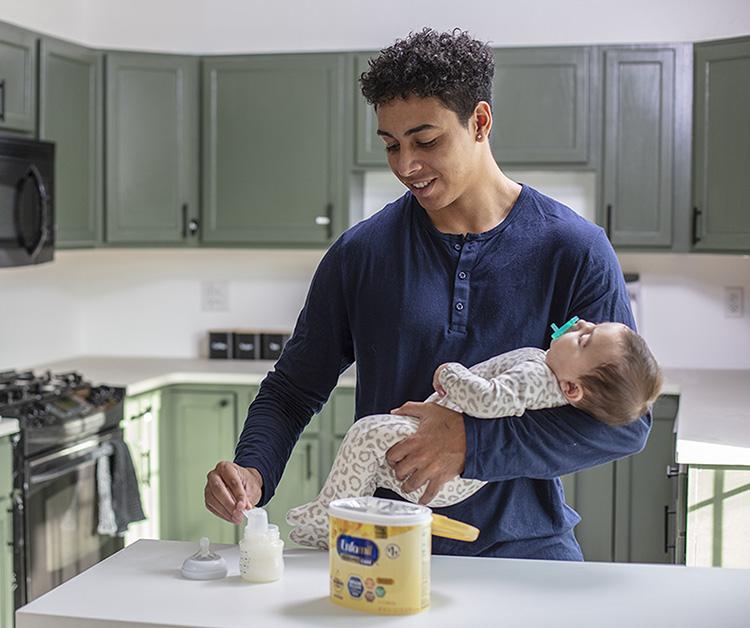 Dad preparing bottle while cradling newborn
