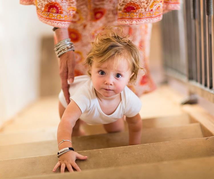 Toddler boy crawling up the stairs as his mom follows behind him