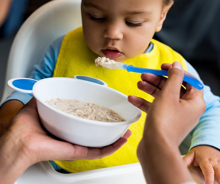 Mom spoon-feeding toddler son in high chair