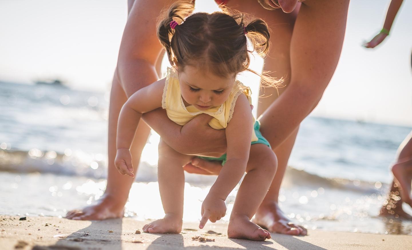 Toddler girl playing in the sand with parent