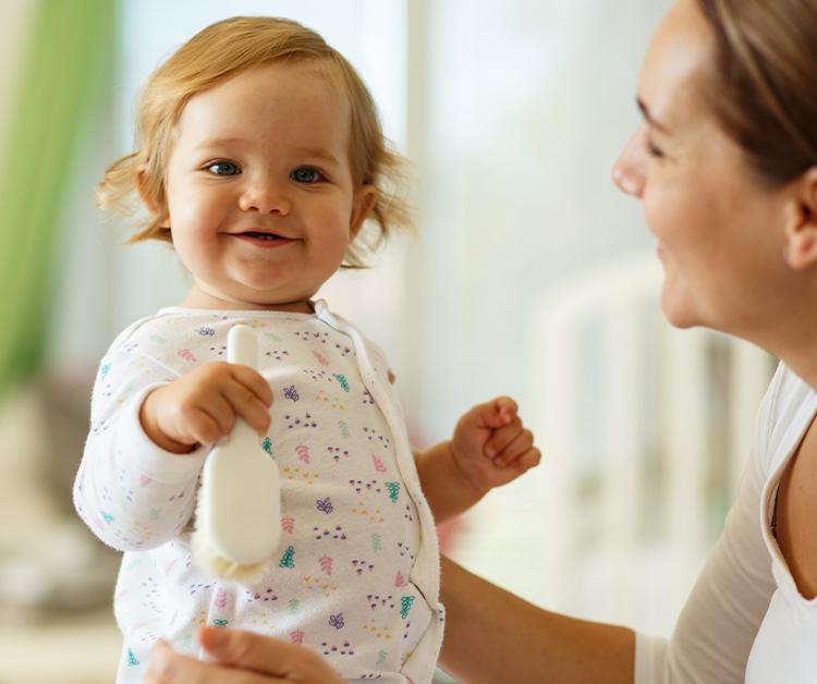 Baby girl holding a hairbrush and her mom is holding her