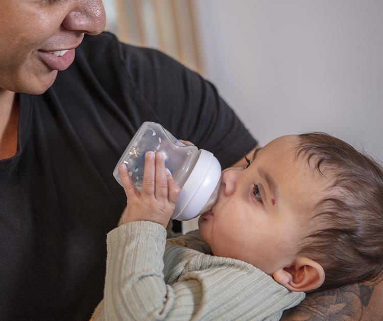 Dad smiling at his baby as the baby holds their own bottle